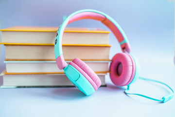 Naklejka premium Stack of books and headphones on a purple background. Audiobook concept. Listen to lessons.