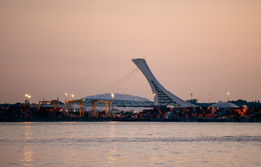 view of an olympic stadium in the distance next to a river on a sunset with a clear sky in summer