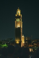 Fototapeta premium view of a tall clock tower next to the water at night with lights on