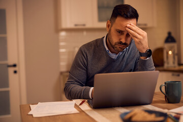 Worried businessman reading problematic email on laptop at home.
