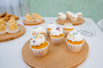 Delicious cupcakes adorned with smooth white frosting and colorful sprinkles sit delightfully arranged on a rustic wooden tray placed on a charming table, ready to be enjoyed