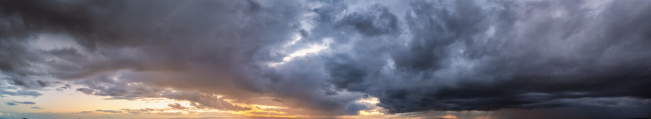 Panorama of a stormy sky with sunlight and dark rain clouds as a texture or background