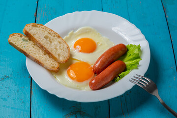 Breakfast fried eggs with sausages, crispy white bread, on a blue table