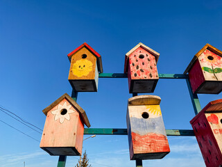 A colorful collection of uniquely designed birdhouses hangs from a sturdy pole, creating an enchanting scene full of charm and whimsical beauty that captivates passersby all day