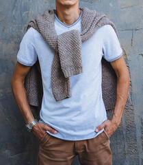 A man, who is stylishly dressed, is standing in front of a blank wall while wearing a cozy sweater...