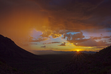 A breathtaking sunset over a vast desert scene, highlighting rugged hills and radiant sunlight breaking through colorful clouds, creating a peaceful and awe-inspiring view of nature's beauty.
