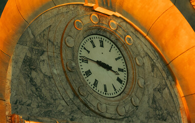 view of a round shape clock with black roman numbers indoor on a stone wall