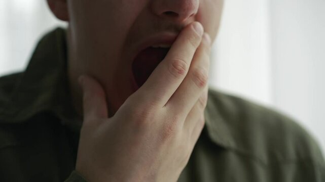 A man covers his mouth with his hand when he yawns.
The man yawns from fatigue.
Bad dream.
The man did not get enough sleep and yawns