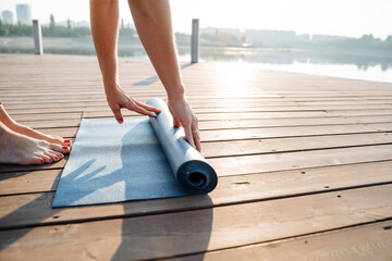 A dedicated woman prepares for yoga by unrolling her mat on a wooden deck overlooking serene water, embracing the tranquility and beauty for a refreshing morning practice