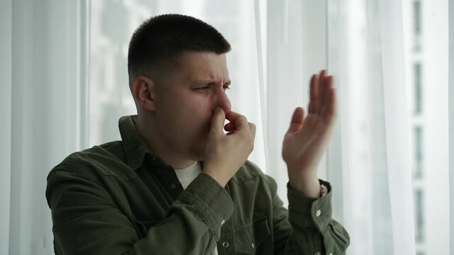 The man gestures that it stinks very strongly.
The stench is strong and the man feels sick.
A man covers his nose from the strong stench.
Someone spoiled the air