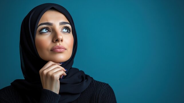 Woman in hijab looks up thoughtfully, displaying a calm and introspective expression in a serene setting