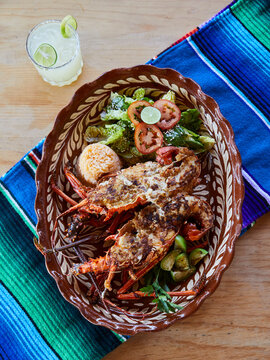 Top view of a plate of deep fried lobster with green salad and rice, over a zarape, and margarita drink.