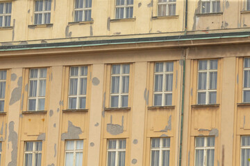The weathered facade of a historic building showcases multiple windows set against a vibrant urban city background