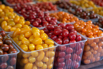 Fresh cherry tomatoes in containers are sold at the vegetable market, in different colors, yellow, brown, red, orange.