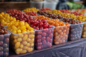 Fresh cherry tomatoes in containers are sold at the vegetable market, in different colors, yellow, brown, red, orange.