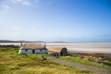 Traditionally white cottage with thatched roof, next to the turquoise bay.North Uist, Scotland