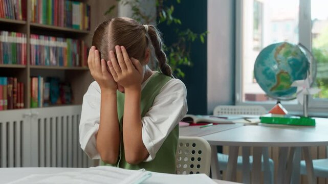 Crying desperate exhausted Caucasian little girl child kid schoolgirl anxious depressed student pupil rubbing eyes cry reading book doing homework trouble mistake mental health studying indoor school