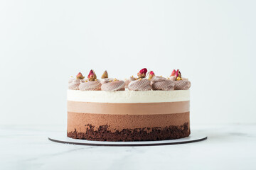 Homemade cake three chocolates on the white marble background. Chocolate souffle cake with sponge cake and three layers of chocolate mousse decorated with whipped cream and dried flowers