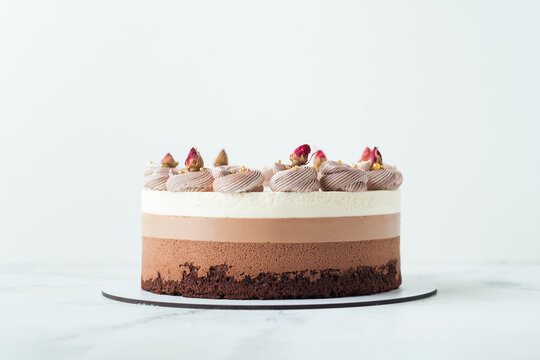 Homemade cake three chocolates on the white marble background. Chocolate souffle cake with sponge cake and three layers of chocolate mousse decorated with whipped cream and dried flowers