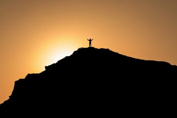 Silhouette of a person standing on top of a mountain at sunset