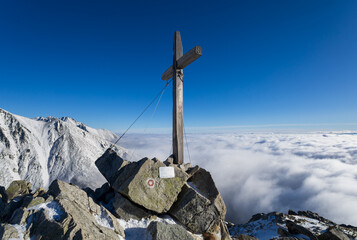 Predne Solisko, High Tatras, Slovakia. Cross on the top, peak and summit of the mountain. Winter nature and religious monument and landmark. Sunny blue sky above clouds, temperature inversion.