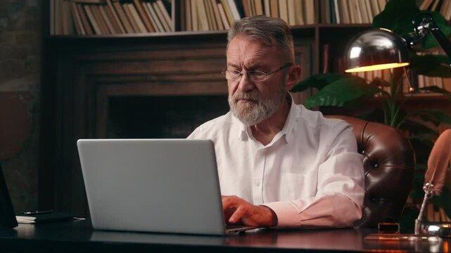 Caucasian old elderly man typing laptop desktop computer working online internet e-business mature male businessman business home office project senior email message indoors entrepreneur e-commerce