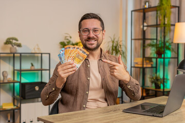 Young businessman freelancer holding fan of cash money euro banknotes, pointing and showing thumbs...