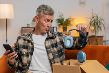 Unhappy young Caucasian man guy unpacking carton box, feeling dissatisfied with getting damaged...