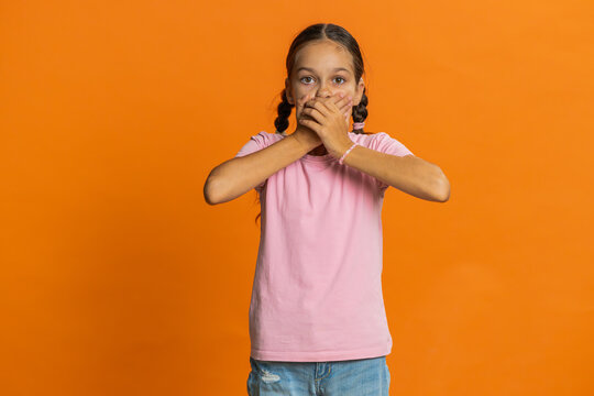 I will not say anything. Frightened strict young preteen child girl kid closing mouth with hands, looking intimidated scared at camera gestures no, refusing to tell terrible secret unbelievable truth.
