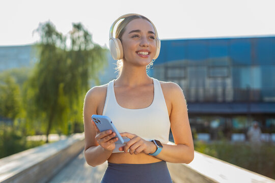 Athletic fitness sport runner girl training exercise, holding smartphone listening music on headphones dancing having fun. Workout cardio in park. Young woman jogger enjoying dance. Active sportswoman - Powered by Adobe