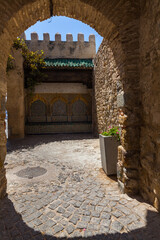 a stone archway, leading towards a courtyard adorned with colorful tiles and overlooked by a...
