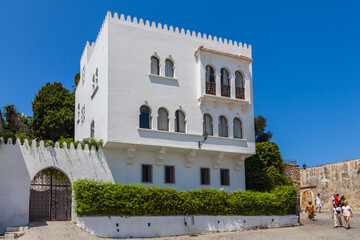 Obraz premium whitewashed building with a distinctive architectural style, featuring arched windows, a flat roof, and a surrounding garden, creating a picturesque Mediterranean scene