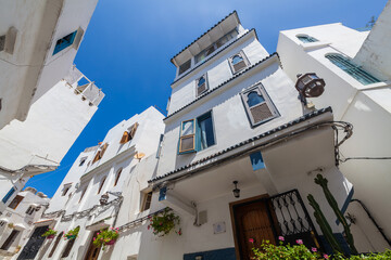 Fototapeta premium dramatic upward perspective of a narrow street lined with whitewashed buildings featuring intricate architectural details, creating a captivating scene against a vibrant blue sky