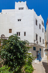 whitewashed building with distinctive architectural features, partially obscured by lush green foliage, against a backdrop of a clear blue sky, creating a charming Mediterranean town scene
