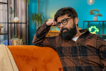 Thoughtful Hispanic man sitting at home looks pensive nervous thinks over life concerns or...