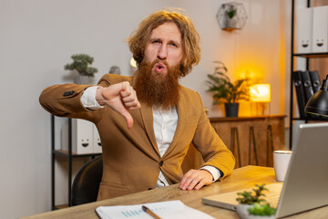 Dislike. Upset Caucasian businessman working on laptop computer at home office showing thumbs down...