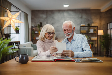 Senior couple sit at a wooden table and look family photos album