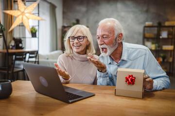 Senior couple excited open a gift while have video call on laptop