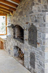 Fototapeta premium Stone barbecue firewood, open brick oven for cooking kebabs and other dishes on fire indoors in backyard. Restaurant kitchen, pizza oven and bar-b-q grill. Cooking food. Interior modern construction