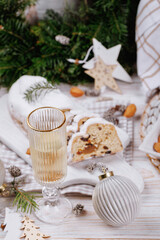 A close-up of a champagne glass with sparkling wine surrounded by slices of traditional stollen bread, pinecones, Christmas ornaments, and a festive holiday table arrangement.