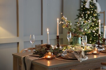 Christmas table setting with stylish dishware, glasses and burning candles in festive decorated room