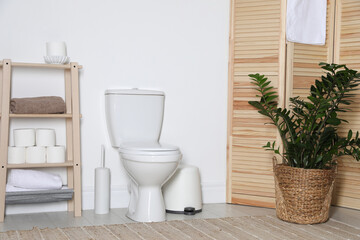 Folding screen, toilet bowl and houseplant in restroom. Interior design
