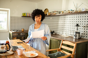 Woman reading bills with laptop on kitchen desk
