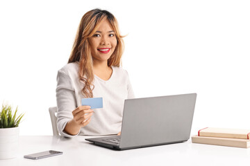 Asian woman holding a credit card and sitting at a desk with a laptop computer