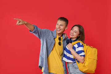 Traveller with backpack. Happy woman and man pointing at something on red background