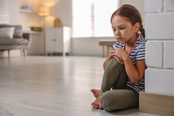 Fototapeta premium Orphanage concept. Sad girl sitting on floor indoors