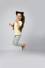 Cute girl with painted face and ears as cat jumping on grey background, space for text