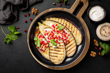 Top view of Roasted, grilled Eggplant with Tahini Yogurt Sauce and pomegranate on a black table surface.