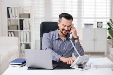 Naklejka premium Happy banker talking on phone at table in office
