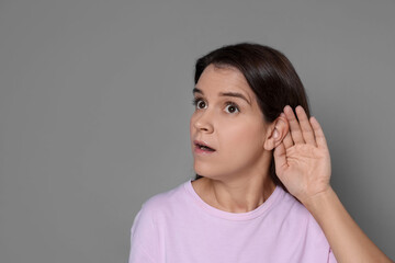 Woman showing hand to ear gesture on grey background, space for text
